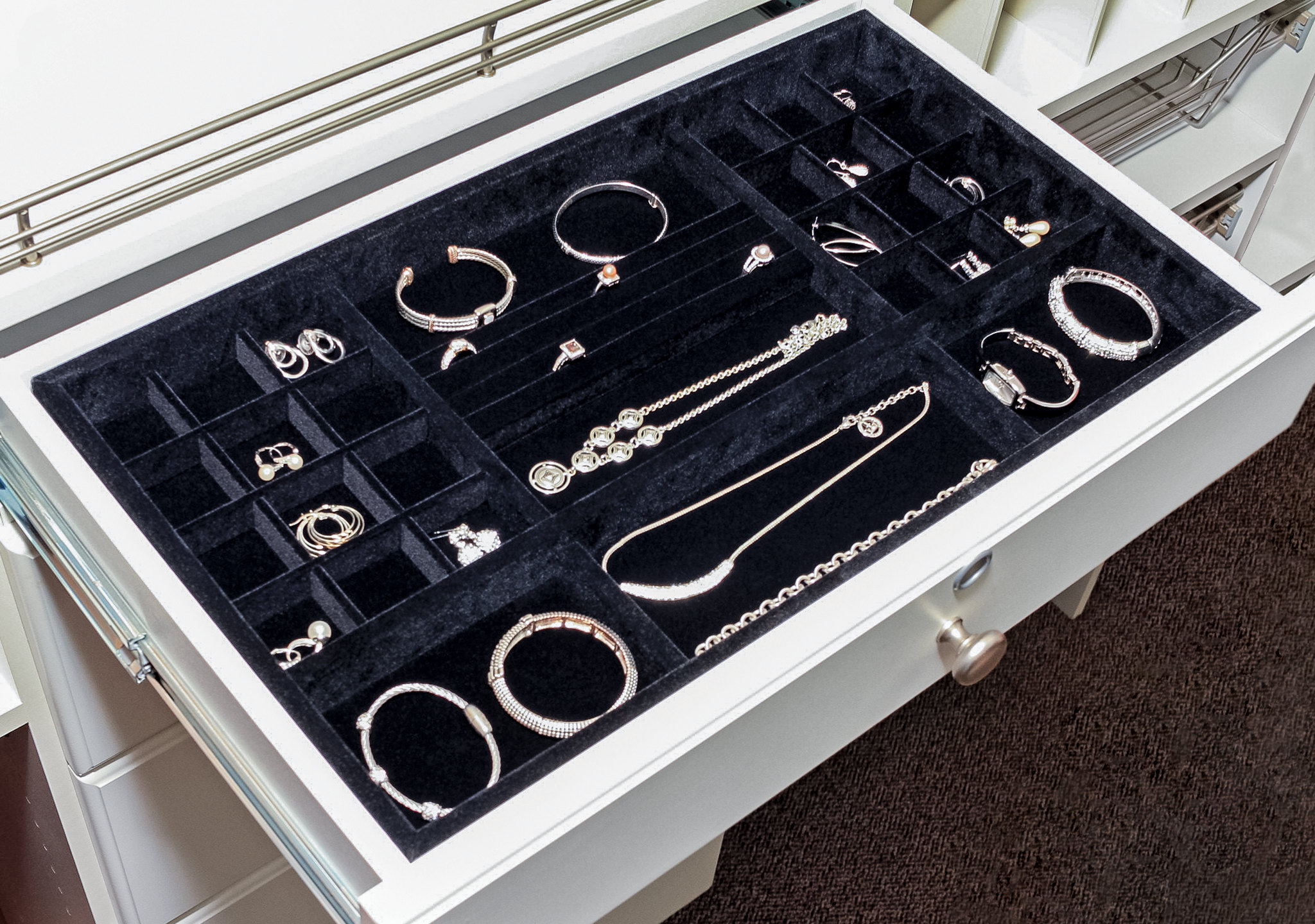 A direct overhead view of a custom closet drawer equipped with a full black velvet jewelry tray insert, compartmentalized to perfectly organize a large collection.