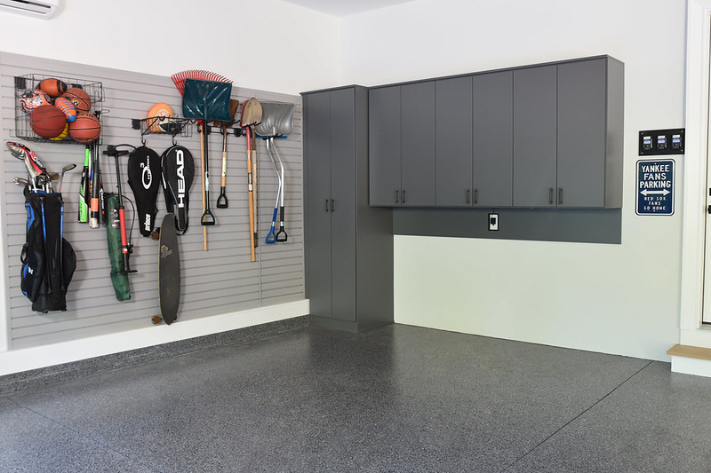 Organized garage with grey cabinets, sports gear, and tools on a wall rack. Sign reads "Yankee Fans Parking." Clean and tidy atmosphere.