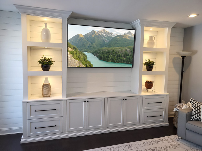 White built in entertainment wall unit with display shelves and a flatscreen TV in the center space.